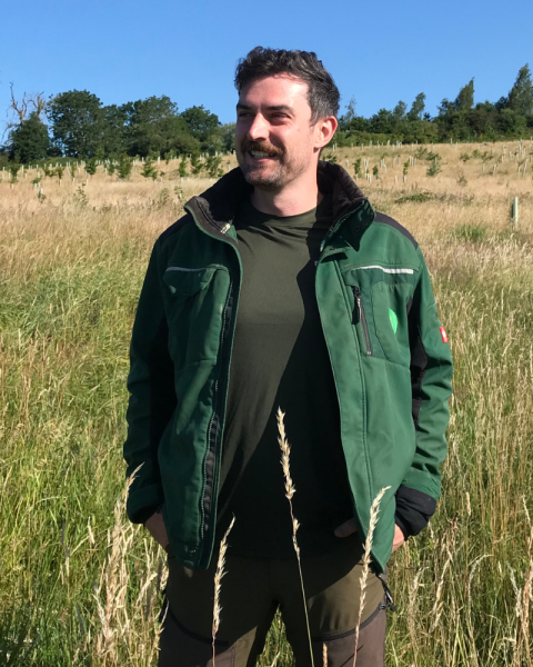 Fletcher stood in a field smiling and looking to his right in to the distance