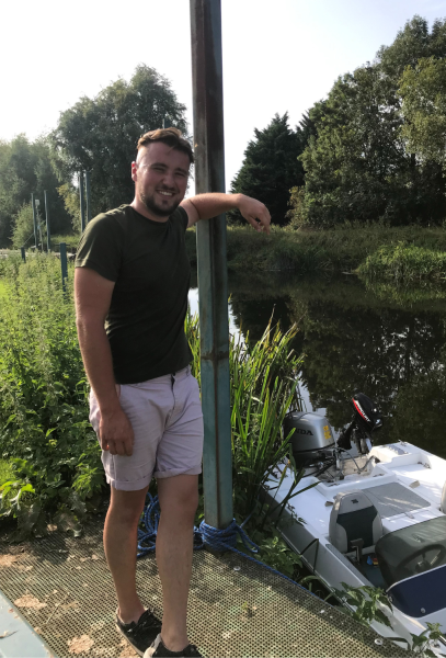 JJ resting against a moorings post with boats in the background at Dovecote