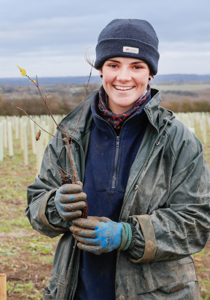 Mel smiling whilst holding a sapling during a tree planting session.