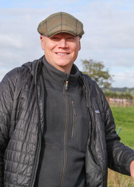 Forest Habitats Manager Tom standing outside wearing a cap with grass and a tree in the background