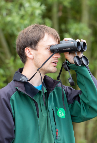 Sam using a pair of binoculars to look for butterflies on a survey