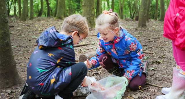 A couple of children crouched down together being creative in the woodland at Middle Spernal