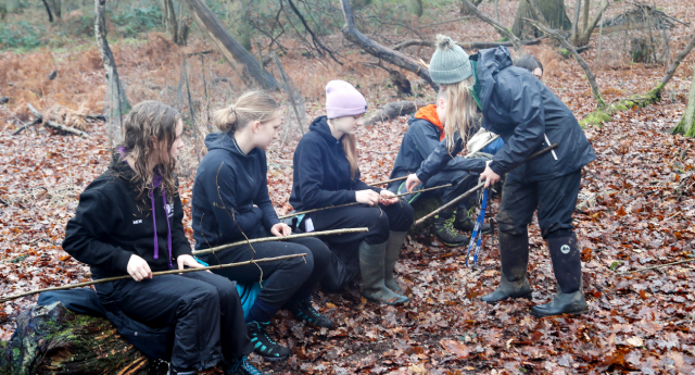 A group of Young Foresters sat on a log together using tools at Middle Spernal with a member of staff