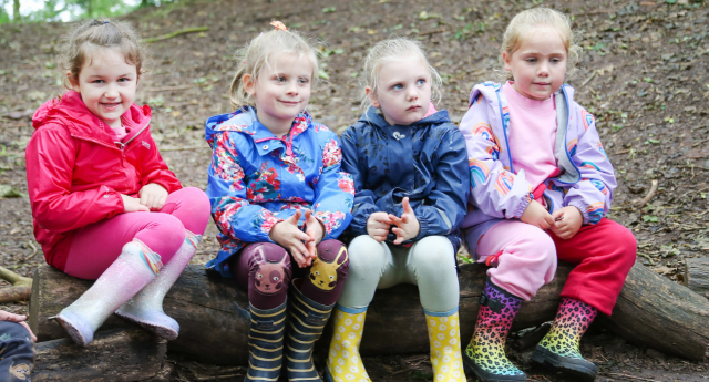 A group of child sat together on a log in the woodland at Gorcott Hill