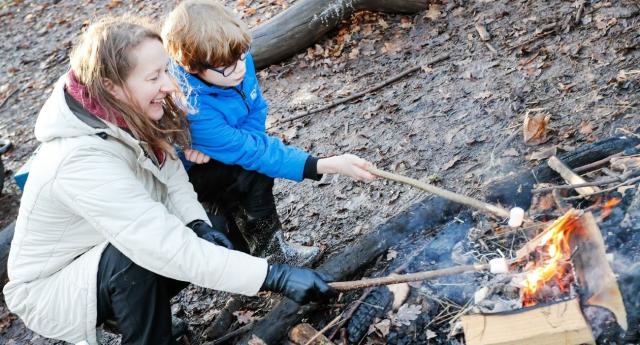 A mum and son toasting marshmallows over a campfire in a Forest clearing