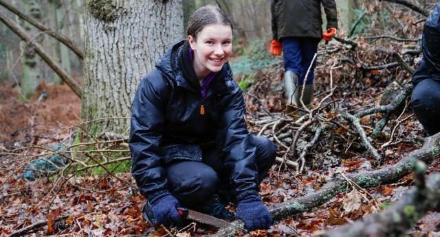 A young person crouching on the forest floor and smiling at the camera during a Young Foresters session in the Forest