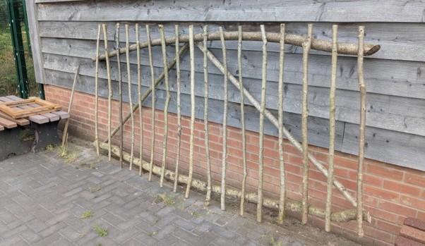 A palisade fence constructed of Hazel timber leaning against a wood cladded wall.